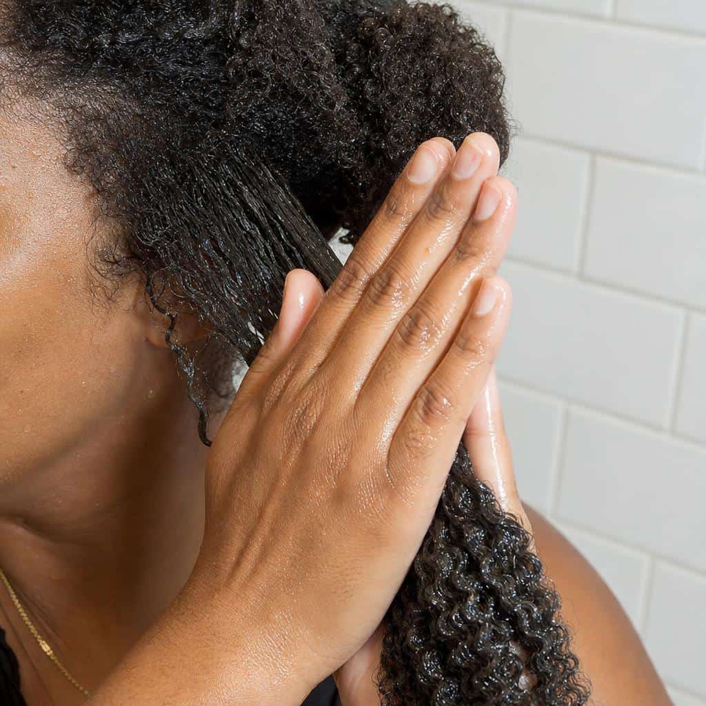 Hands applying gel to wet 4A hair using praying hands method for coil definition